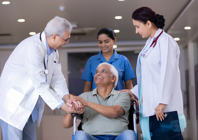 A male doctor, a female doctor, and a nurse attending to a smiling elderly man sitting in a wheelchair at a hospital.