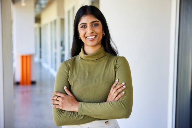 Portrait of a confident businesswoman smiling while standing with her arms crossed in the bright hallway of a modern office